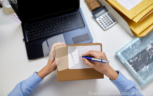 Image of close up of hands filling form on parcel at office