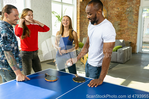 Image of Young people playing table tennis in workplace, having fun