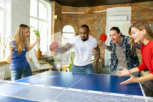 Image of Young people playing table tennis in workplace, having fun