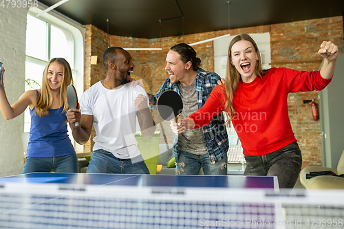 Image of Young people playing table tennis in workplace, having fun