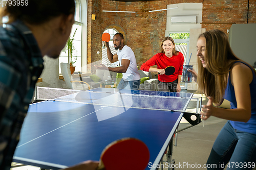 Image of Young people playing table tennis in workplace, having fun