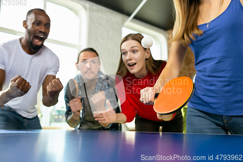 Image of Young people playing table tennis in workplace, having fun