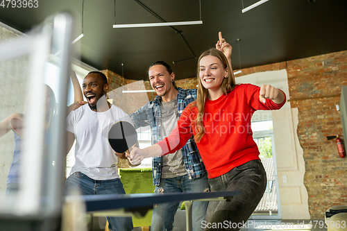 Image of Young people playing table tennis in workplace, having fun