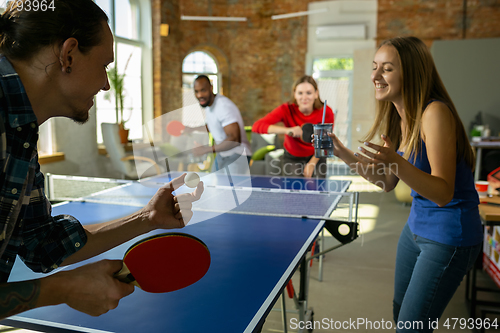 Image of Young people playing table tennis in workplace, having fun