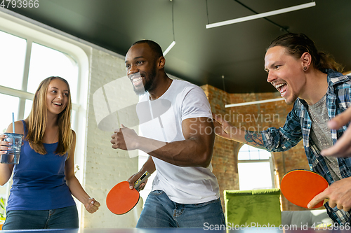 Image of Young people playing table tennis in workplace, having fun