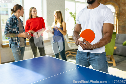 Image of Young people playing table tennis in workplace, having fun