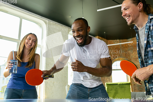 Image of Young people playing table tennis in workplace, having fun