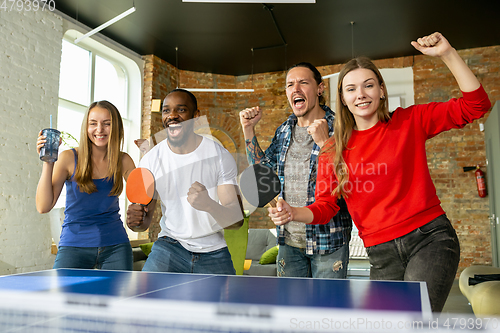 Image of Young people playing table tennis in workplace, having fun