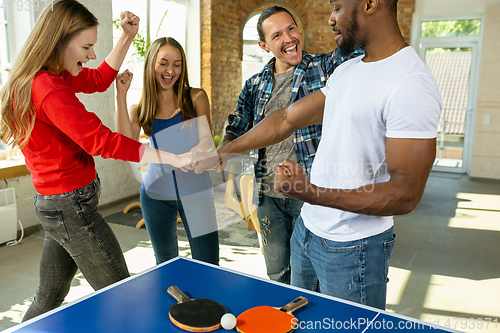 Image of Young people playing table tennis in workplace, having fun