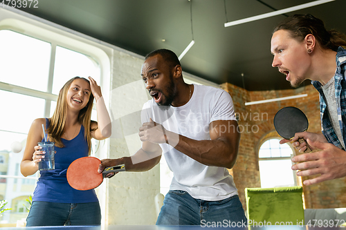 Image of Young people playing table tennis in workplace, having fun