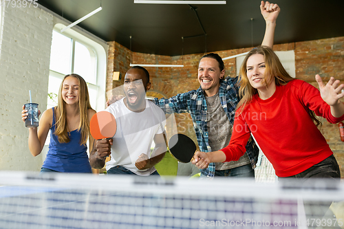 Image of Young people playing table tennis in workplace, having fun