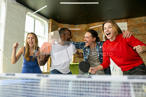 Image of Young people playing table tennis in workplace, having fun