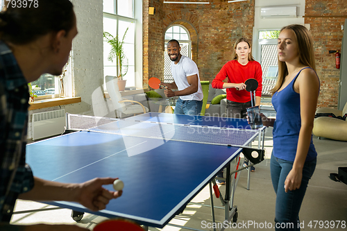 Image of Young people playing table tennis in workplace, having fun