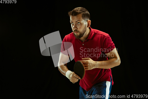 Image of Young man playing table tennis on black studio background