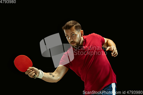 Image of Young man playing table tennis on black studio background