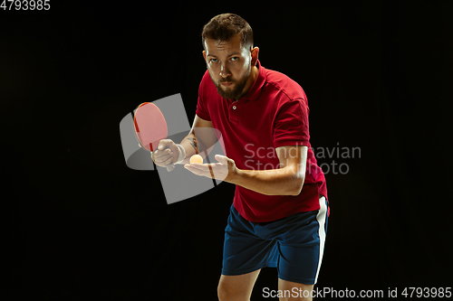 Image of Young man playing table tennis on black studio background