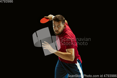 Image of Young man playing table tennis on black studio background