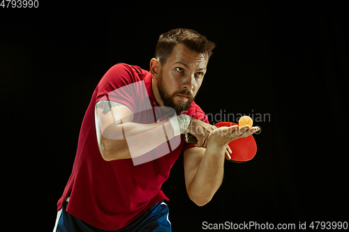 Image of Young man playing table tennis on black studio background