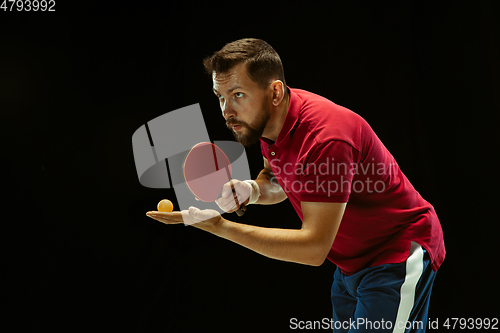 Image of Young man playing table tennis on black studio background