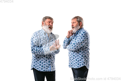 Image of Senior man arguing with himself on white studio background.