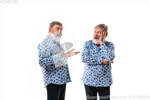 Image of Senior man arguing with himself on white studio background.