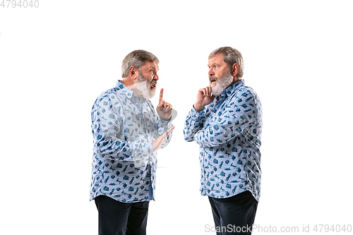 Image of Senior man arguing with himself on white studio background.