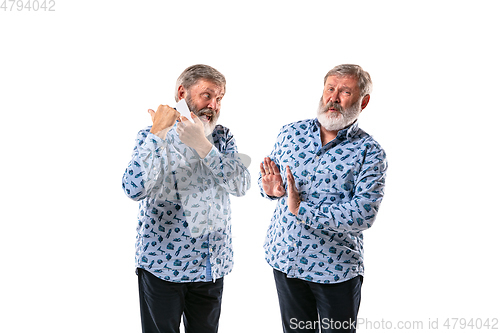 Image of Senior man arguing with himself on white studio background.