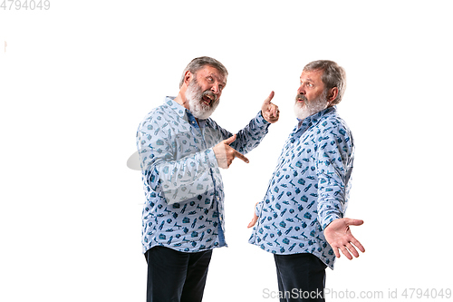 Image of Senior man arguing with himself on white studio background.