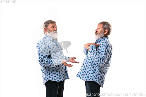 Image of Senior man arguing with himself on white studio background.