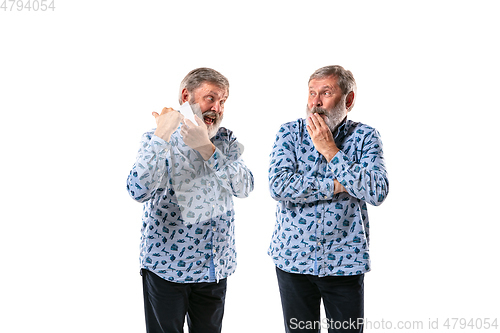 Image of Senior man arguing with himself on white studio background.