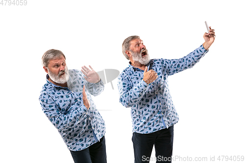 Image of Senior man arguing with himself on white studio background.