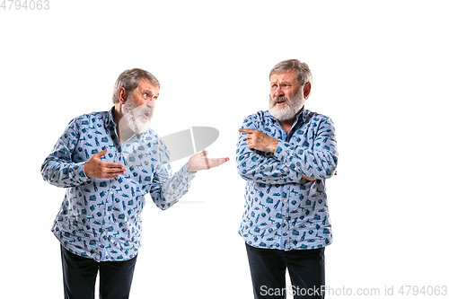 Image of Senior man arguing with himself on white studio background.