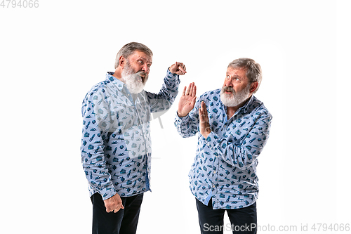 Image of Senior man arguing with himself on white studio background.