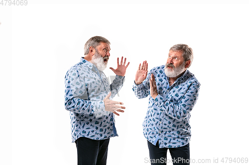 Image of Senior man arguing with himself on white studio background.