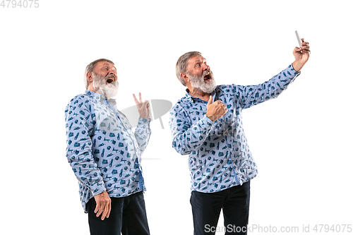 Image of Senior man arguing with himself on white studio background.