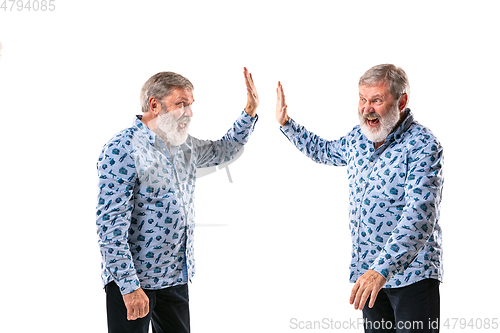 Image of Senior man arguing with himself on white studio background.