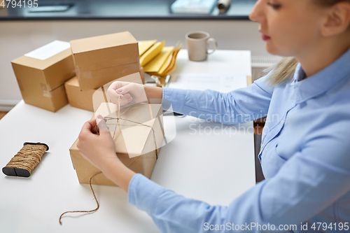 Image of woman packing parcel and tying rope at post office