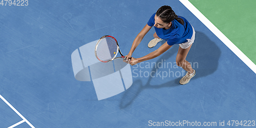 Image of Young woman in blue shirt playing tennis. Youth, flexibility, power and energy.