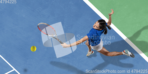 Image of Young woman in blue shirt playing tennis. Youth, flexibility, power and energy.