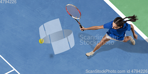 Image of Young woman in blue shirt playing tennis. Youth, flexibility, power and energy.