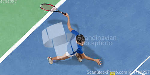 Image of Young woman in blue shirt playing tennis. Youth, flexibility, power and energy.