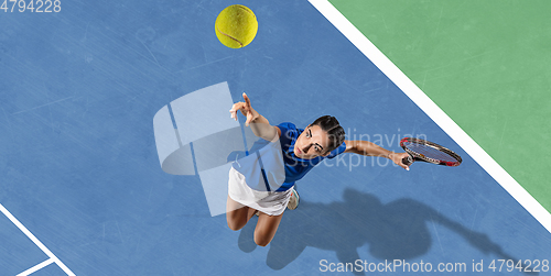 Image of Young woman in blue shirt playing tennis. Youth, flexibility, power and energy.