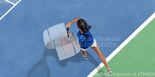 Image of Young woman in blue shirt playing tennis. Youth, flexibility, power and energy.