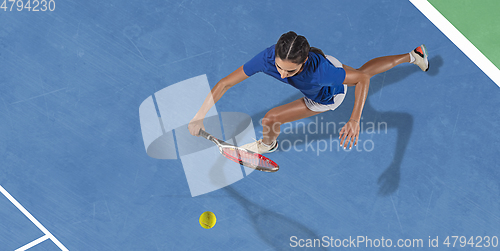 Image of Young woman in blue shirt playing tennis. Youth, flexibility, power and energy.