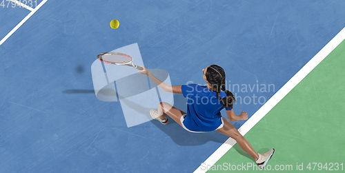 Image of Young woman in blue shirt playing tennis. Youth, flexibility, power and energy.