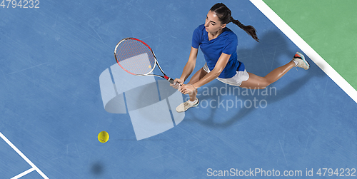 Image of Young woman in blue shirt playing tennis. Youth, flexibility, power and energy.