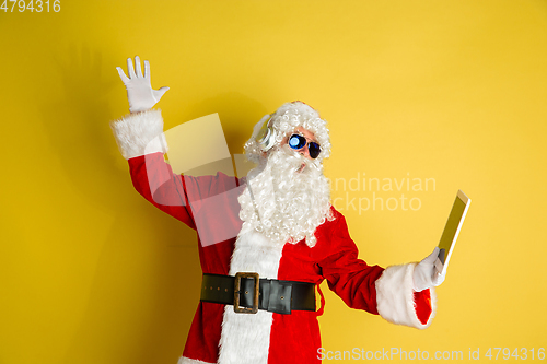 Image of Santa Claus with modern gadgets isolated on yellow studio background