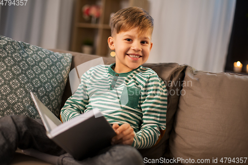 Image of happy smiling little boy reading book at home