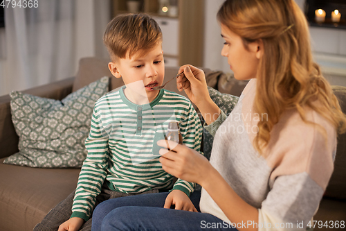 Image of mother giving medication or cough syrup to ill son