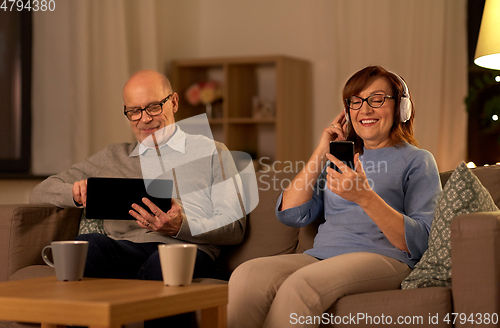 Image of happy senior couple with gadgets at home